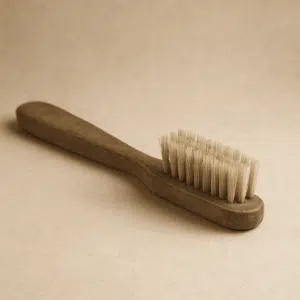 Sepia-toned photograph of a vintage manual toothbrush with wooden handle and natural bristles before toothbrushes were modernized.