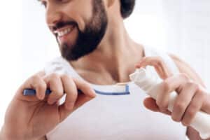 Close up. Bearded smiling man squeezes toothpaste onto toothbrush. Hygiene concept. Morning procedures. 
