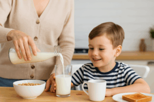 Parent pouring A2 milk from a glass bottle into a child’s glass at the breakfast table, with cereal and toast nearby in a bright family kitchen.